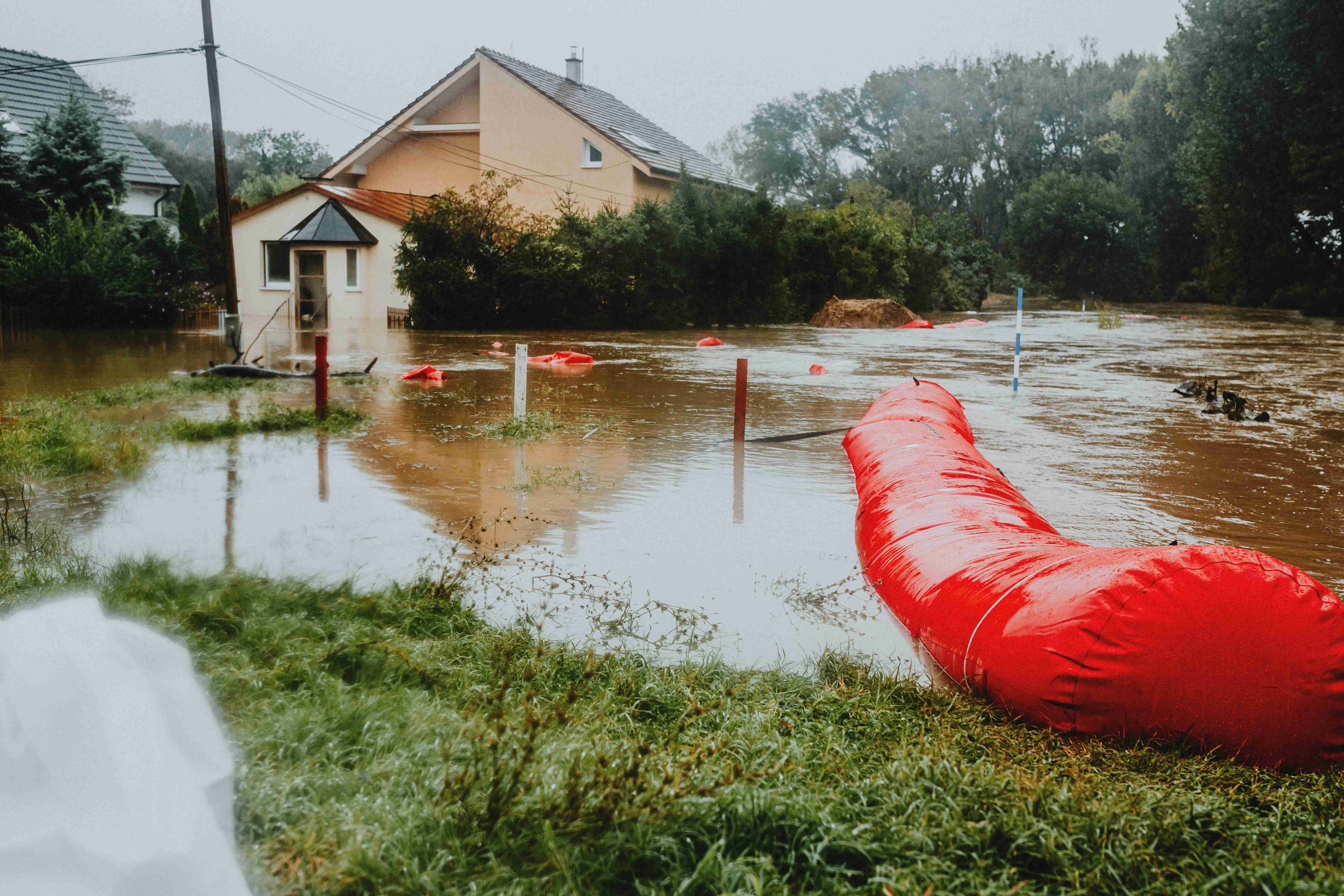 Überflutetes Wohngebiet mit Hochwasser und roten Schutzbarrieren. 